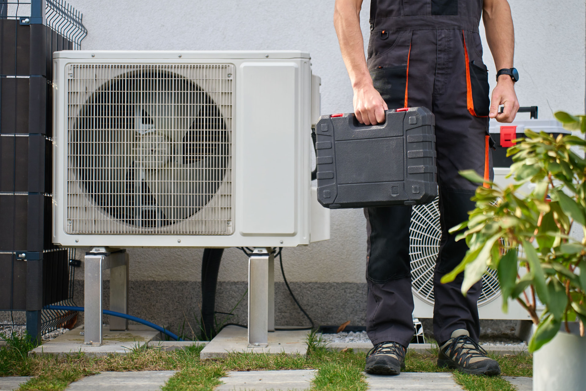 Engineer carrying a toolbox beside an outdoor heat pump